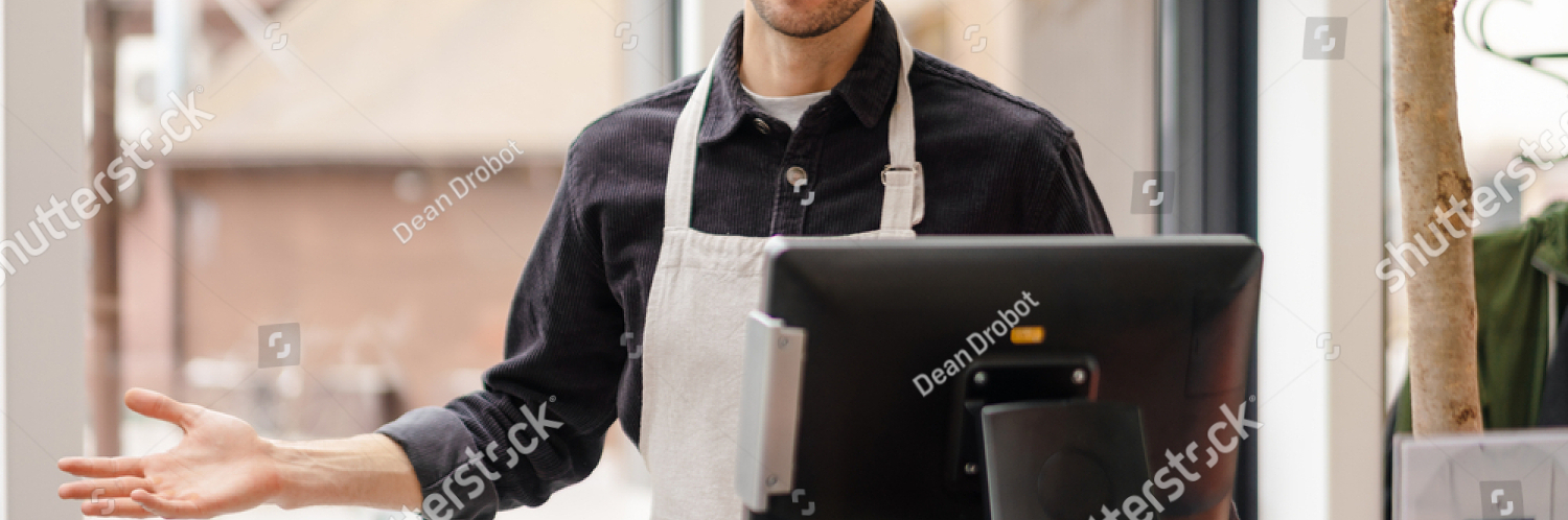 stock photo smiling young man in apron standing at the cash register indoors 1960671214